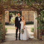 Bride and groom standing under floral archway.