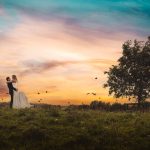 Couple embraces under vibrant sunset sky with birds.