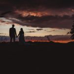 Couple holding hands at sunset in a field.