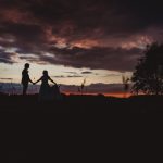 Couple holding hands at sunset, silhouetted against sky.