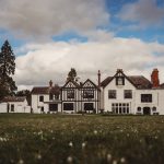 Historic manor house with garden, under cloudy sky.