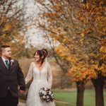 Bride and groom walking in autumn parkland.