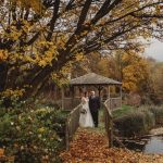 Bride and groom on leafy autumn bridge.