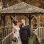 Bride and groom smiling under wooden gazebo.