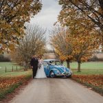 Bride, groom, blue Beetle under autumn trees.