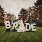 Bride and bridesmaids holding large white letters outdoors.