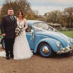 Bride and groom with vintage blue car in countryside.