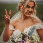 Bride smiling with bouquet, peace sign gesture.