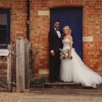 Wedding couple outside Bassmead Manor door, smiling together.