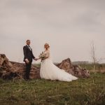 Couple in wedding attire by large log outdoors.