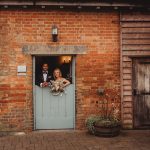 Bride and groom in rustic doorway with bouquets.