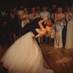 Bride and groom kissing on dance floor, guests cheering.