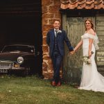 Bride and groom holding hands by vintage car.