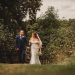 Newlyweds walking hand in hand through greenery