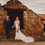 Bride and groom smiling at rustic stone building