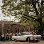 Wedding car outside historic church with guests gathered