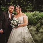 Wedding couple in garden, holding bouquet.