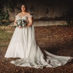 Bride in white dress holding bouquet outdoors.