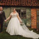 Bride and groom smiling in front of rustic shed.