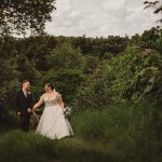 Bride and groom walking in lush green garden.