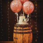 Wedding cake on barrel with decorative balloons.