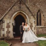 Bride and groom standing by a stone church entrance.