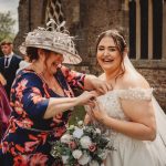 Bridesmaid assists bride with dress outside church.