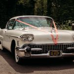 Classic white wedding car with red ribbons