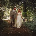 Bride and groom walking through forest path.