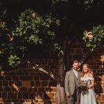 Bride and groom under tree by brick wall