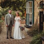 Couple in wedding attire by rustic house.