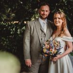 Bride and groom in forest, smiling with bouquet.