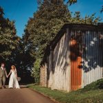 Bride and groom walking by rustic barn, countryside.