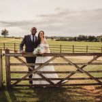 Couple posing by a rustic wooden gate at wedding.