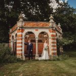 Bride and groom by brick garden pavilion.