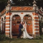 Bride and groom by brick archway.