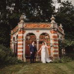 Bride and groom holding hands by brick structure