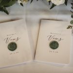 Wedding vow books on table with greenery.