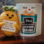 Crochet pineapple toy with positive message, next to mug.