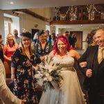 Bride walking down aisle, smiling with guests.