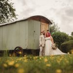 Couple posing by rustic wooden hut in garden.