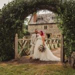 Newlyweds under garden arch at stone house