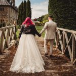 Bride and groom walking on rustic bridge.