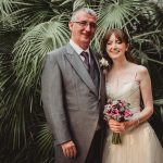 Bride and groom smiling under lush green foliage.