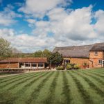 Rural brick barn with garden under blue sky.