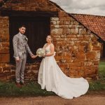 Bride and groom holding hands by stone building.