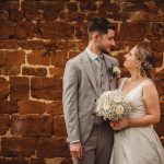 Bride and groom smiling against rustic brick wall.