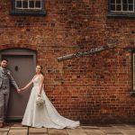 Couple holding hands outside brick cottage door.