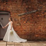 Bride and groom holding hands by brick cottage.