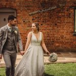 Bride and groom walking near brick cottage.